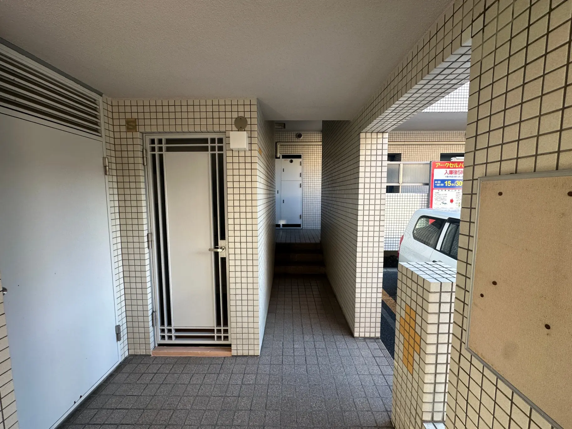 タイル張りのアパートエントランス、クリアガラスのドア、屋内駐車場が見える光沢のある床