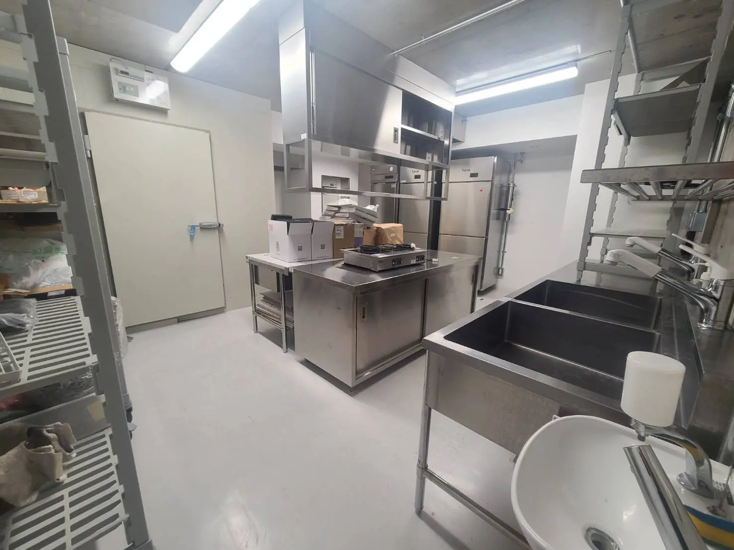 清潔で整理されたレストランの厨房、ステンレス製の調理設備、シンク、そして収納棚が備わったプロフェッショナルなキッチンインテリア