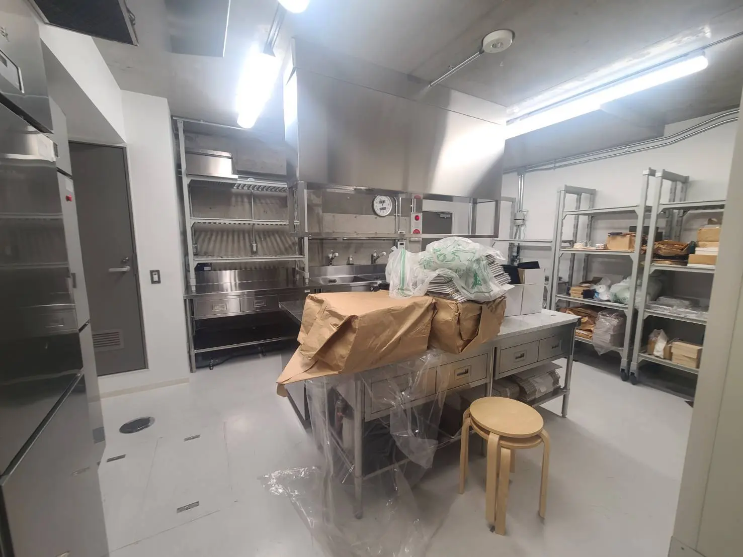プロ仕様の商業キッチン、ステンレス製作業台と器具、包装資材が置かれた清潔感のある調理スペース
