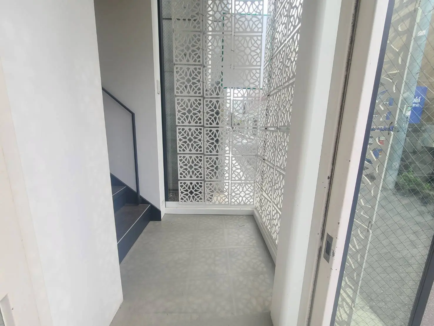 モダンなデザインの白いエントランスホール、装飾的なカットアウトパネルの扉、タイルの床