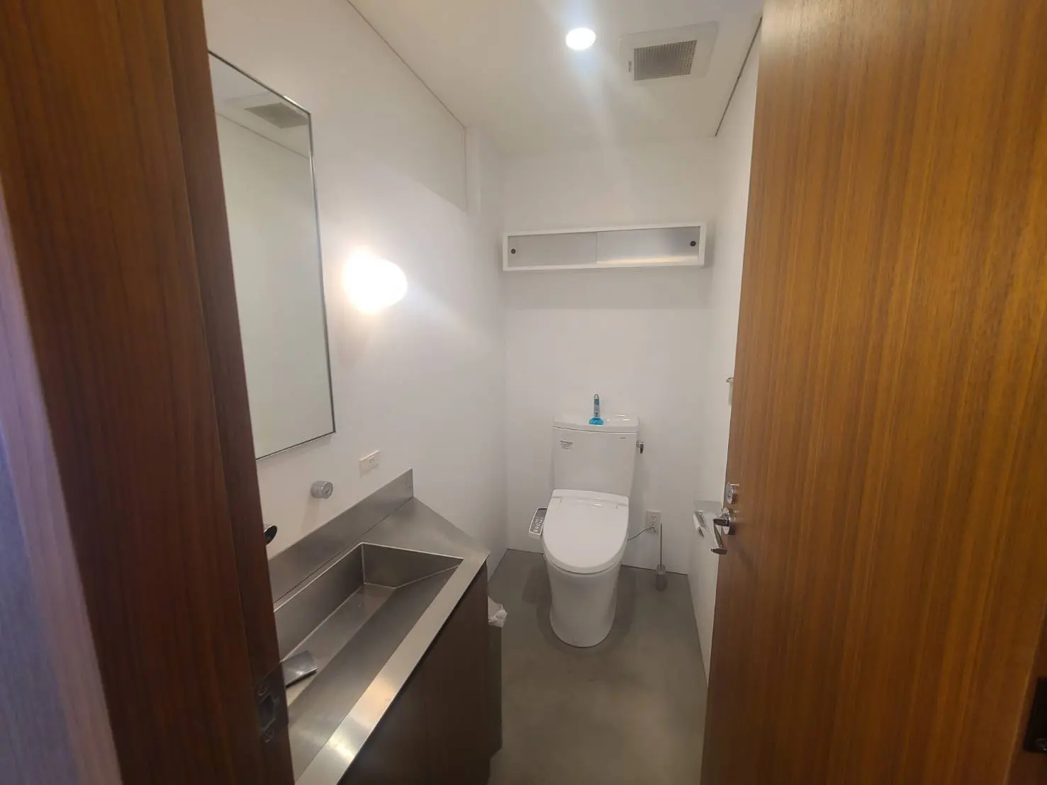 シンプルなデザインのトイレと手洗い場、壁掛けミラーと白熱灯、木目調のドアのインテリア