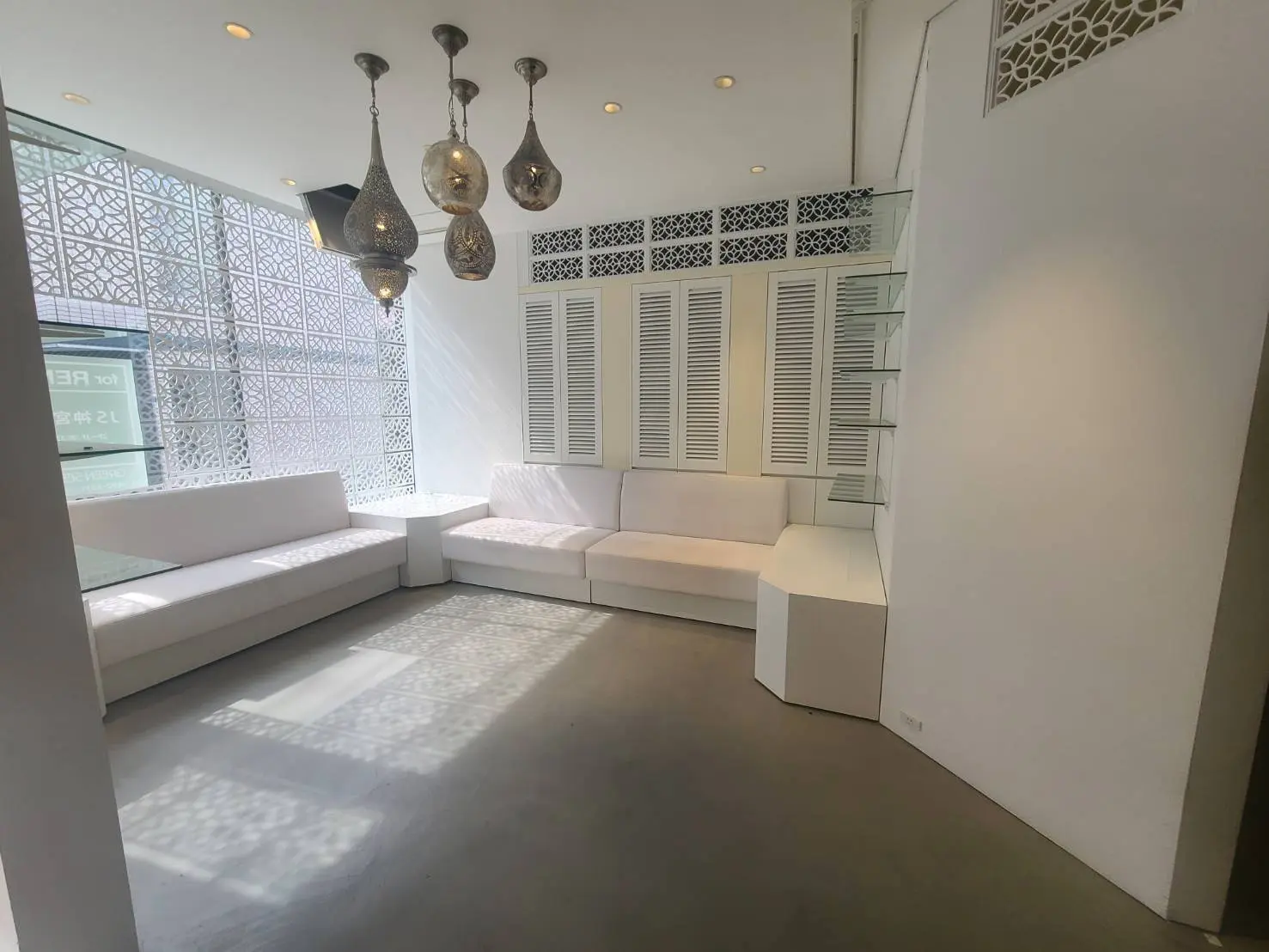 ミニマリストデザインの応接室、アラビックスタイルの窓、モダンな吊りランプ、白いソファと清潔感のあるインテリア