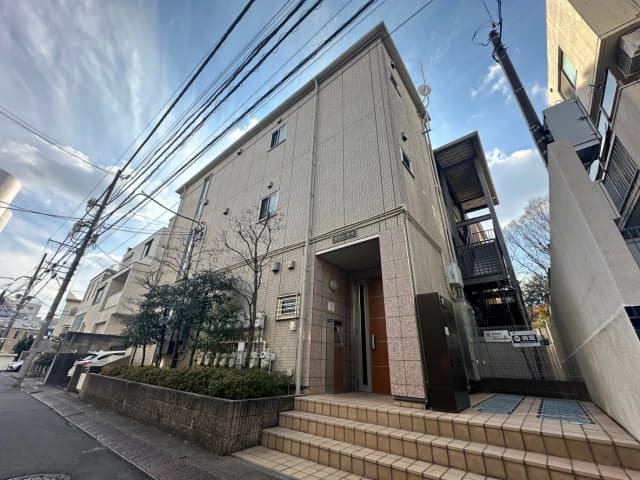 都市の住宅街にある現代的なアパートの外観、電線が張り巡らされた青空の下