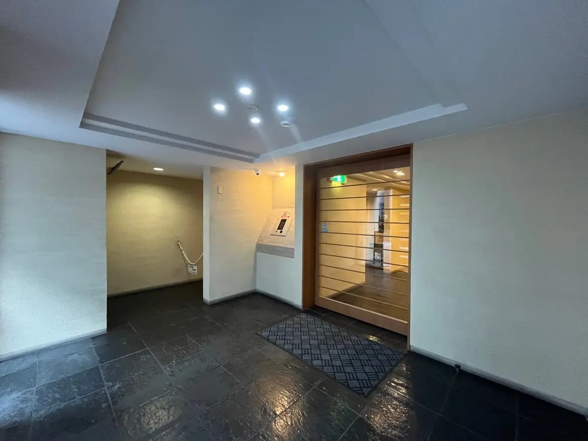 モダンなビルのエントランスホール、黒いタイルの床、木目調のドア、天井にダウンライト