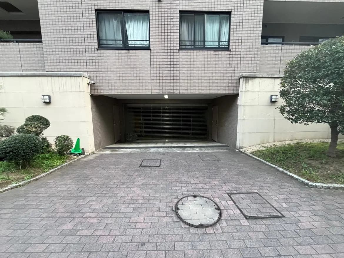 ビルの入り口と地下駐車場のゲート、石畳のアプローチ、緑の植栽