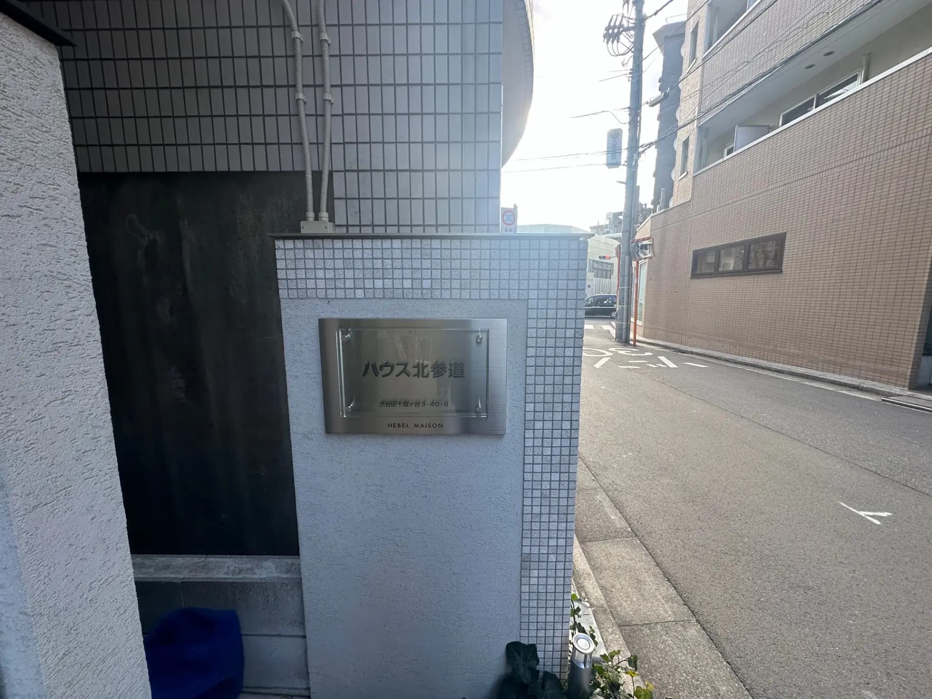 ヘーベルメゾンの建物入口、タイル壁と看板、アスファルト道路と街灯が見える外観