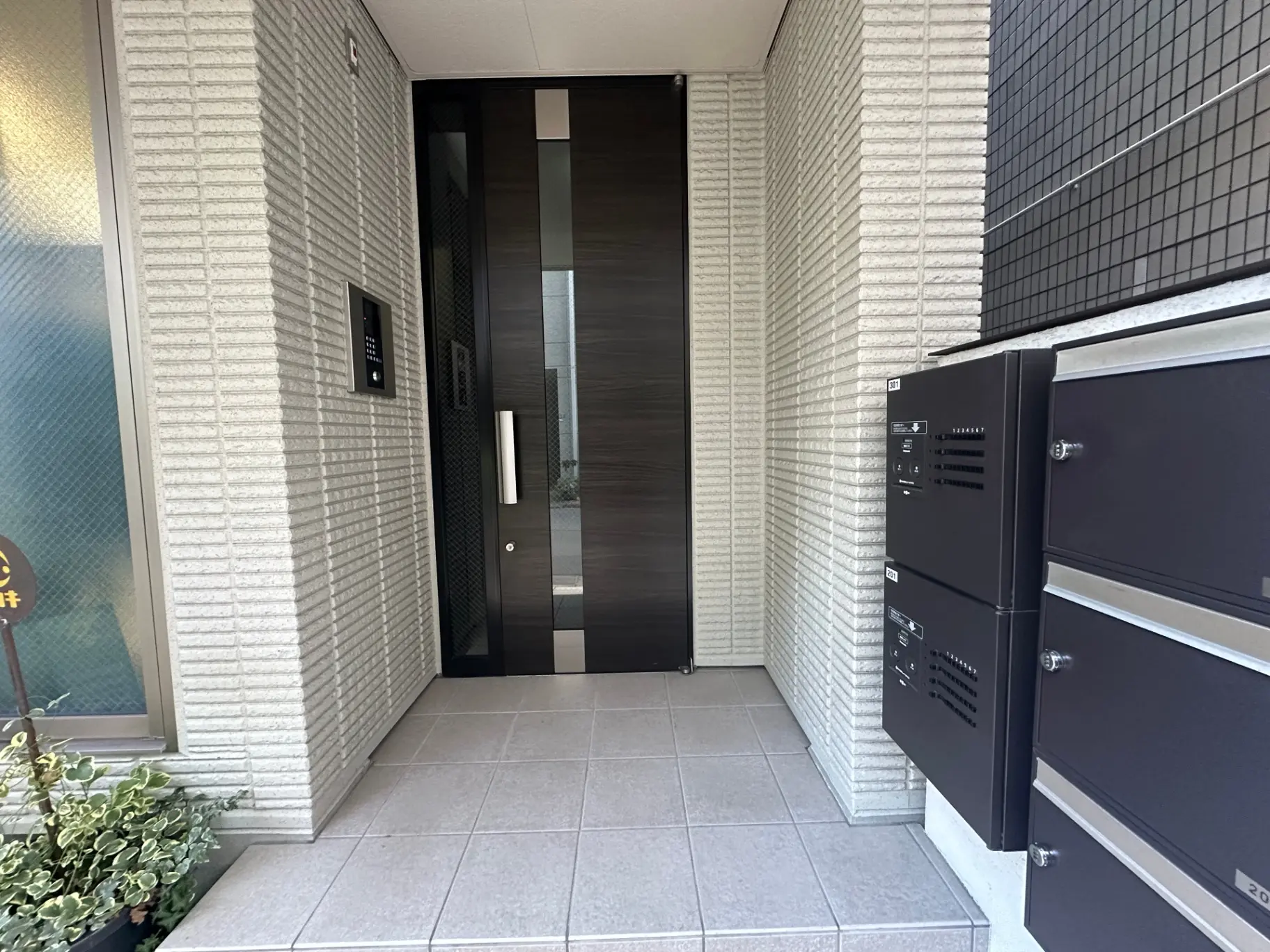 現代的なエントランス、清潔感のあるタイル壁、セキュリティシステム付きの玄関ドア