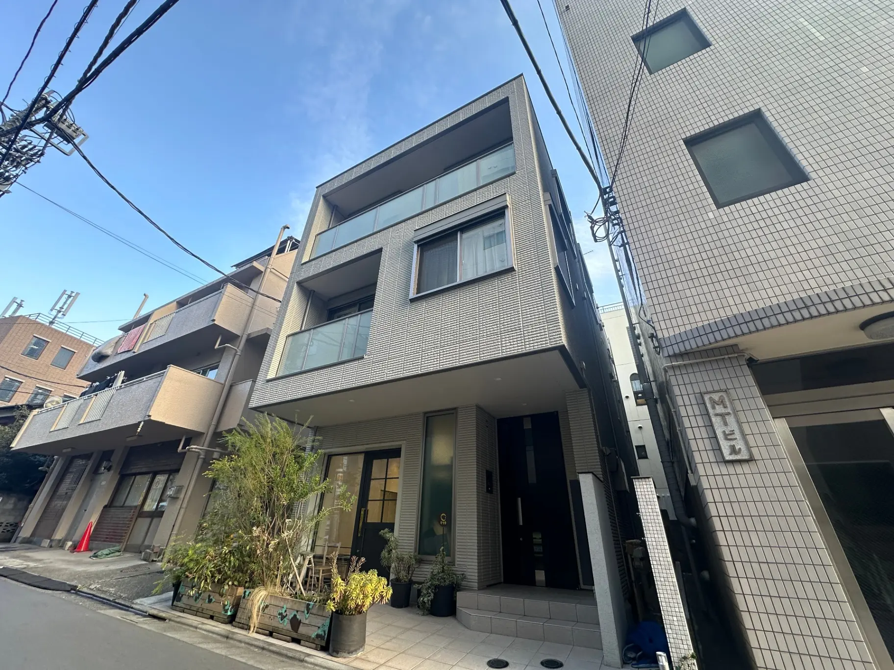 都市型のモダンな外観のアパート、洗濯物が干されているバルコニー、植栽が配されたエントランス