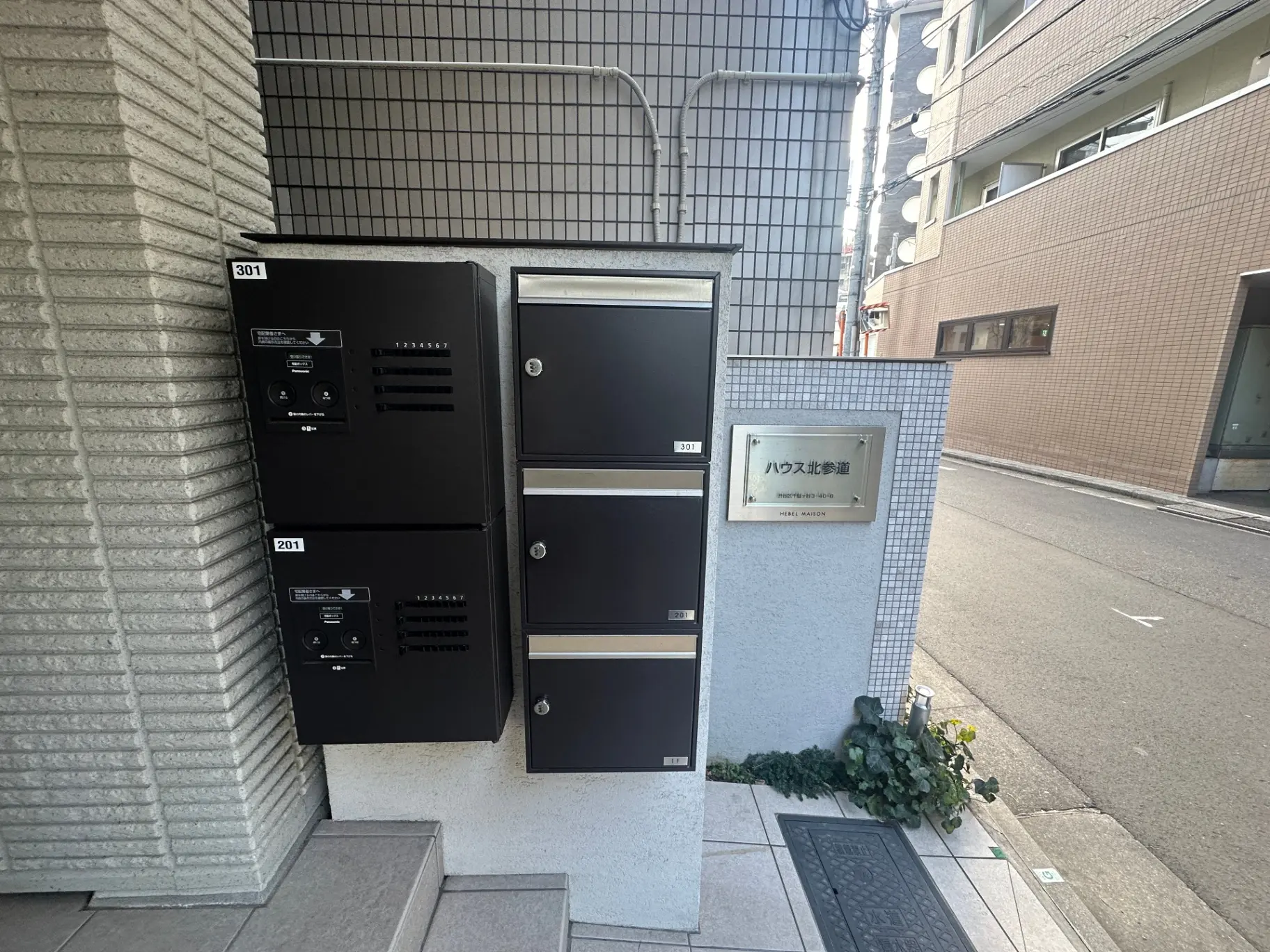 市街地のアパートのエントランス、インターフォンと郵便受け、ハウスメイト清掃の案内プレート