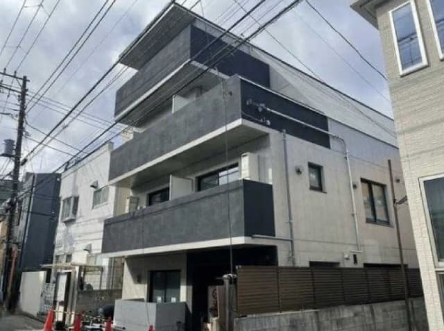 - 現代的なデザインの四階建て住宅、バルコニー付きの外観、周囲に電柱や配線が見える街並み