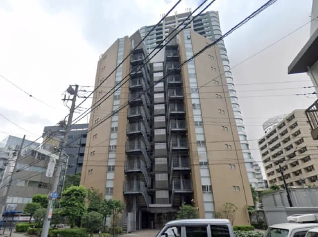 - モダンなデザインのマンションの外観、バルコニー付きの階段と周囲の緑豊かな景観、都市のビル群に囲まれた立地