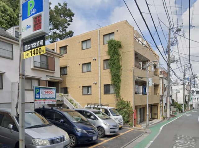 - 駐車場の看板が見える住宅街の風景、近くにアパートと駐車中の車両、電柱と電線が張り巡らされた通りの一コマ
