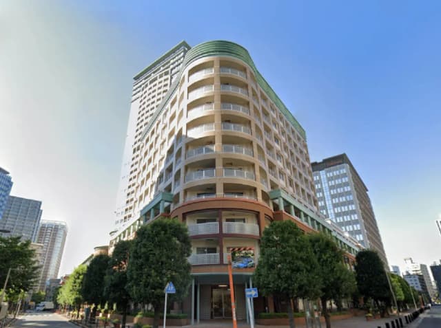 - 現代的なデザインの高層マンション、曲線のバルコニーと周囲の緑が調和した外観、青空の下の街並み