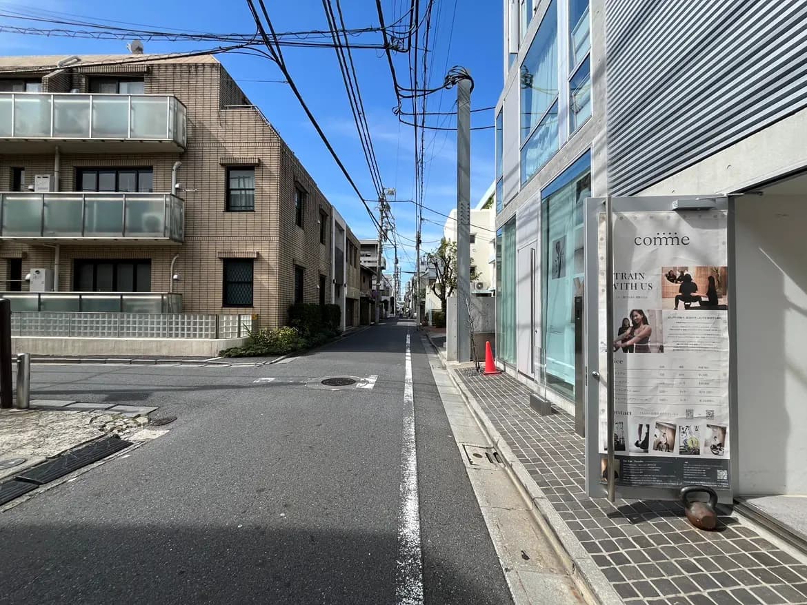 - 静かな街並みに面したフィットネススタジオの入口と近くに立つマンション、青空が広がる街の風景