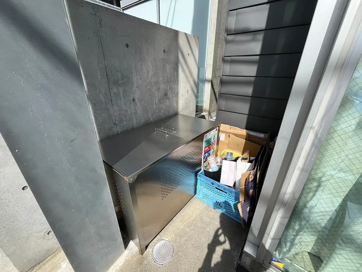 - ステンレス製のゴミ箱と整理された廃棄物、コンクリートの壁に囲まれた屋外の収納スペース