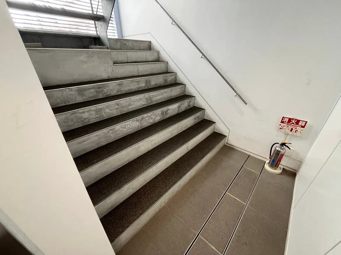 - コンクリート製の階段と滑り止めが施された踏面、手すり、近くに消火器が設置されたエントランスの内部デザイン