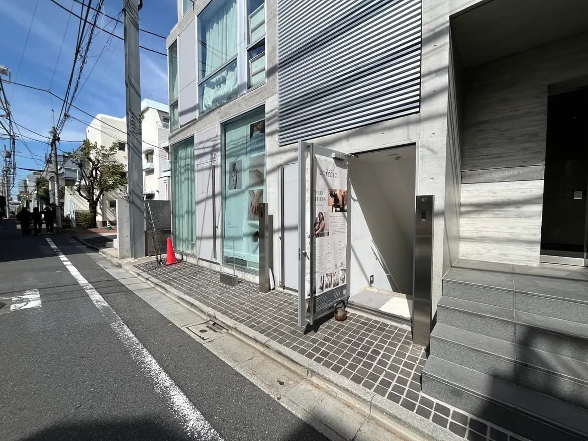 - モダンな建物の入口、ガラスのドアと階段、周囲には電柱や街路樹がある風景