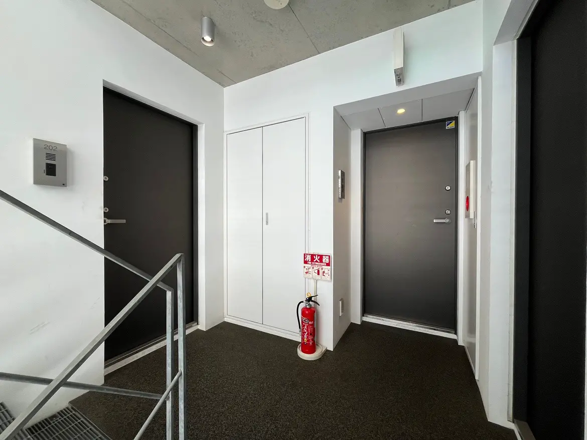 - シンプルでスタイリッシュなエントランスホール、ブラックドアの前にある消火器とセキュリティインターホンが配置された空間