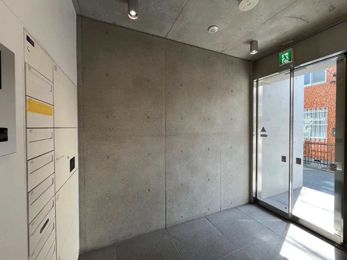 - コンクリートの壁とモダンなエントランス、郵便受けとガラス扉から自然光が差し込む空間