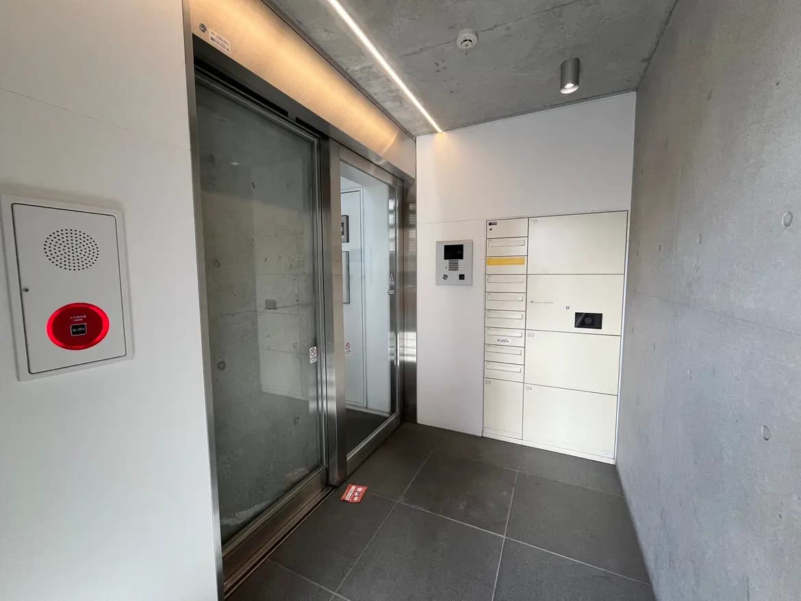 スタイリッシュなエントランスホール、自動ドア、郵便受けとインターフォンが設置されたコンクリートの壁面。