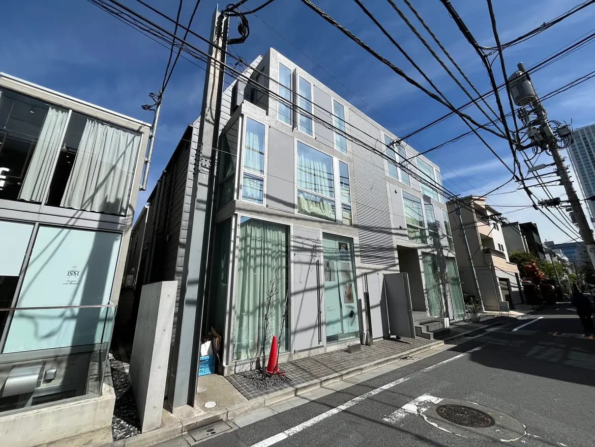 - 現代的なデザインの3階建ての建物、周囲に電柱と電線があり、明るい青空の下に位置する様子