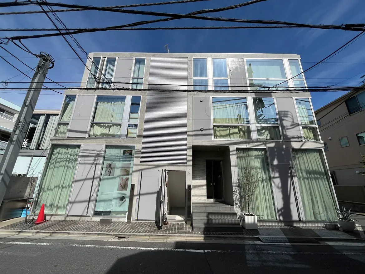 - モダンな外観の三階建てビル、広い窓とカーテン、街中の電線が走る風景