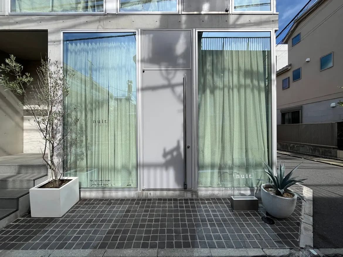 - モダンな建物のエントランス、透明なカーテンと植物が配置された外観、日差しを受けて輝くガラス窓