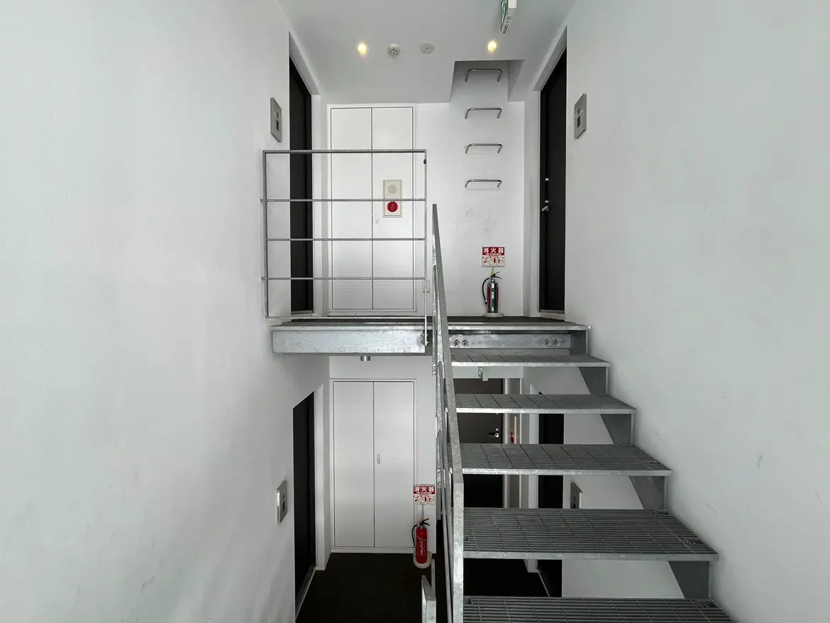 - シンプルなデザインの内階段、白い壁と金属製の手すりが特徴、上階へのアクセスが可能な明るい空間