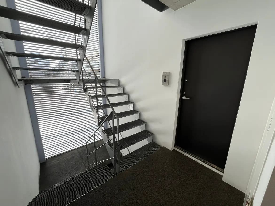 - モダンなデザインの階段と黒いドア、明るい自然光が差し込む住居のエントランスエリア