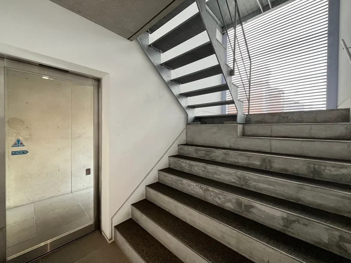 - 現代的なスチール製の階段とエレベーターのドア、明るい自然光が差し込むシャープなデザインの空間