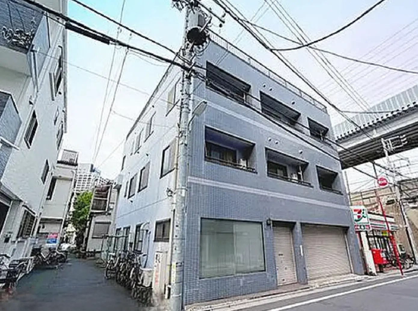 - 青いタイル張りの外観を持つ商業ビル、周囲には自転車が並び、近くにコンビニエンスストアの看板が見える街角の風景