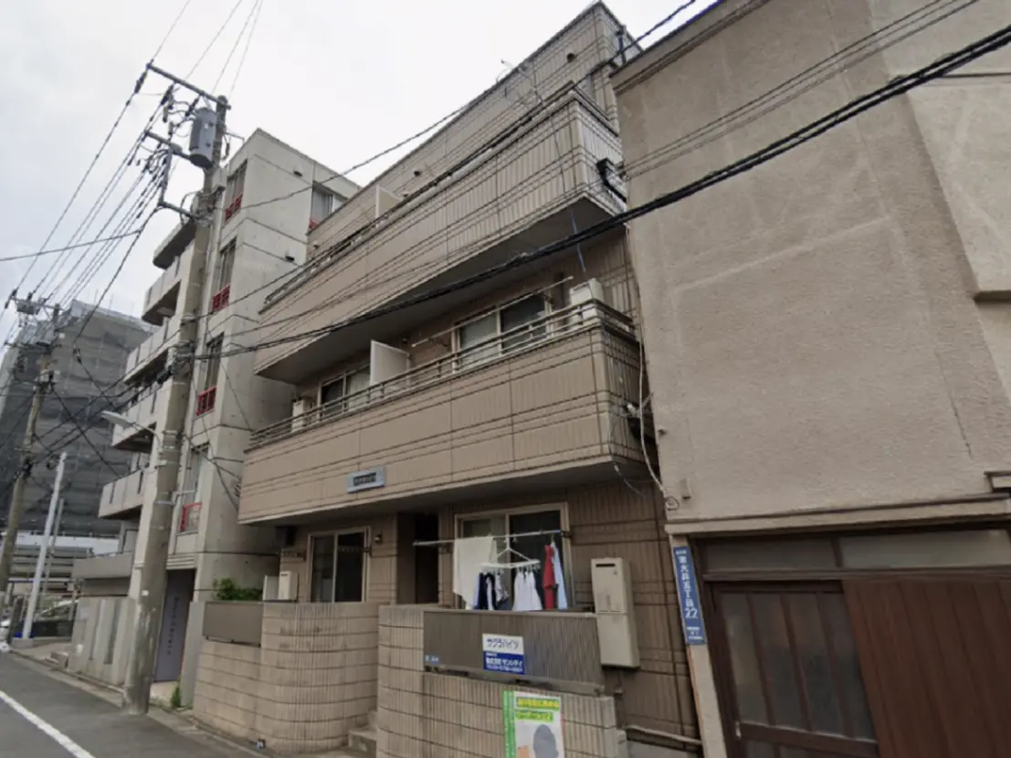 - 街中のアパートメントビル、ベランダには洗濯物が干され、周囲に電柱や電線が見える景観