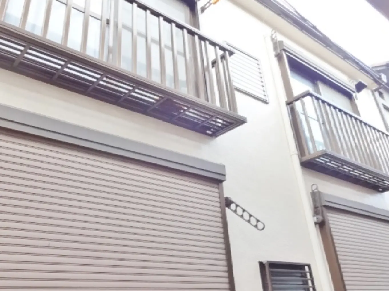 - 二階建ての住宅の外観、バルコニーとシャッター付きの窓があり、白い壁が特徴的なデザイン