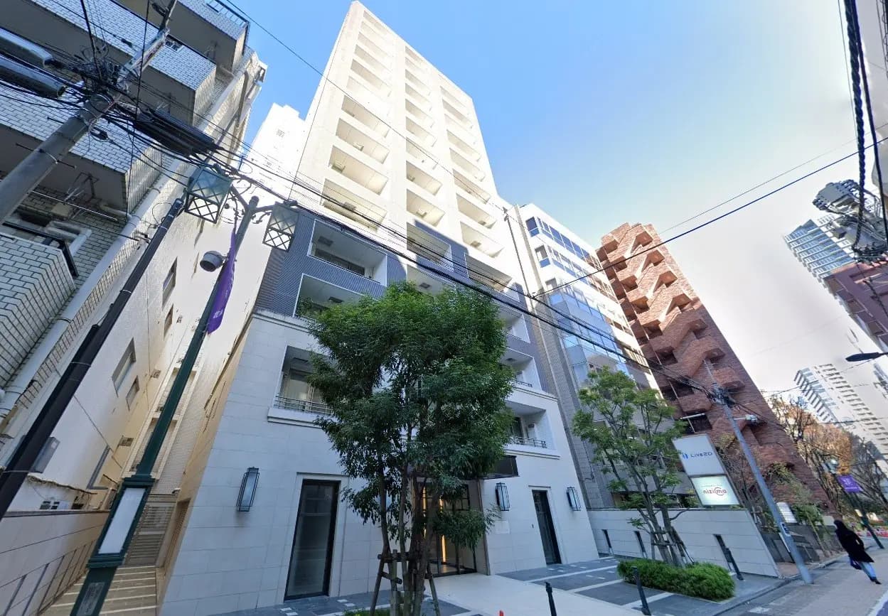 - 都市の風景に溶け込むモダンなマンションの外観、緑豊かな樹木と周囲の高層ビルとのコントラストが印象的な景観