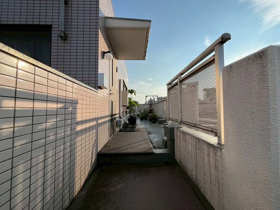 - 高層ビルの屋上に続く、タイル張りの廊下と植栽、青空が広がる午後の光景