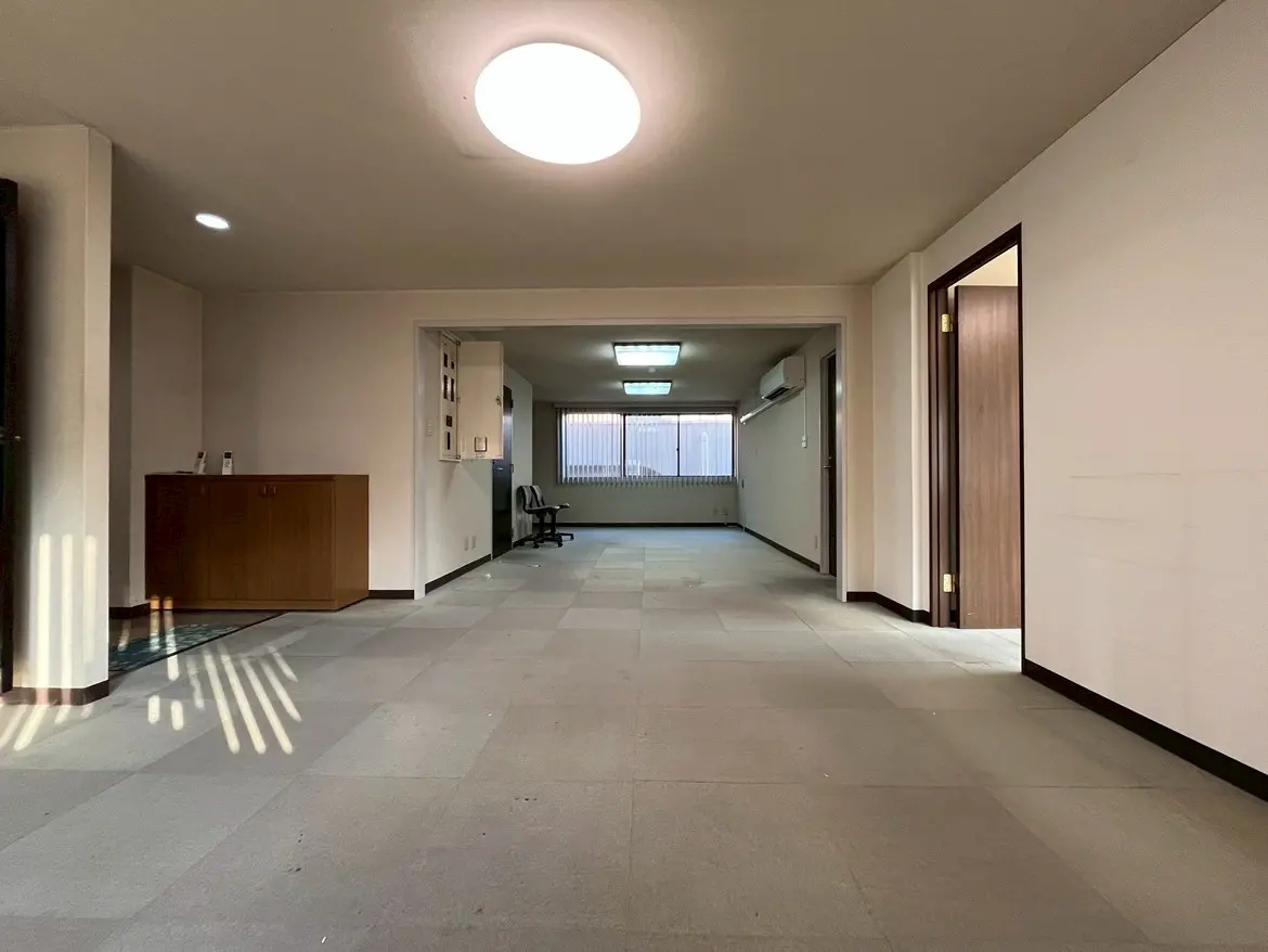 - 明るいリビングルーム、広々とした空間とシンプルなインテリア、壁に木製の収納キャビネットと調整可能な照明、奥にはドアと窓が見える部屋の写真