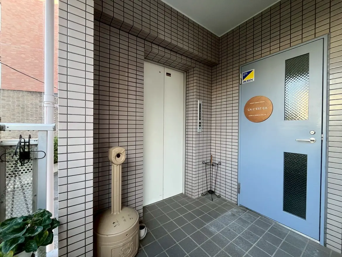 - モダンなデザインのエントランス、タイル張りの壁と窓、電気エレベーターと青色の扉が特徴の玄関前の風景