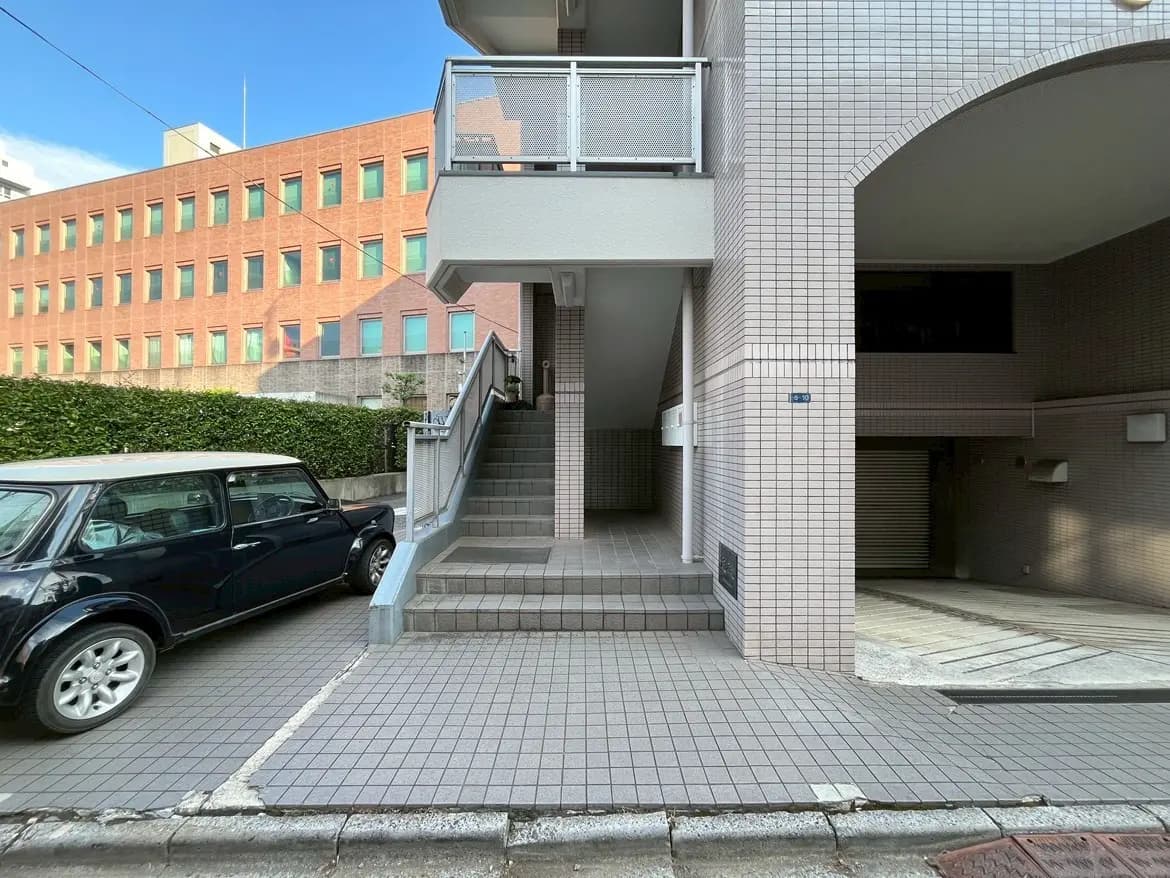 - モダンな建物のエントランス、階段と黒い車が見える道路の風景、明るい空の下にあるタイル張りの歩道