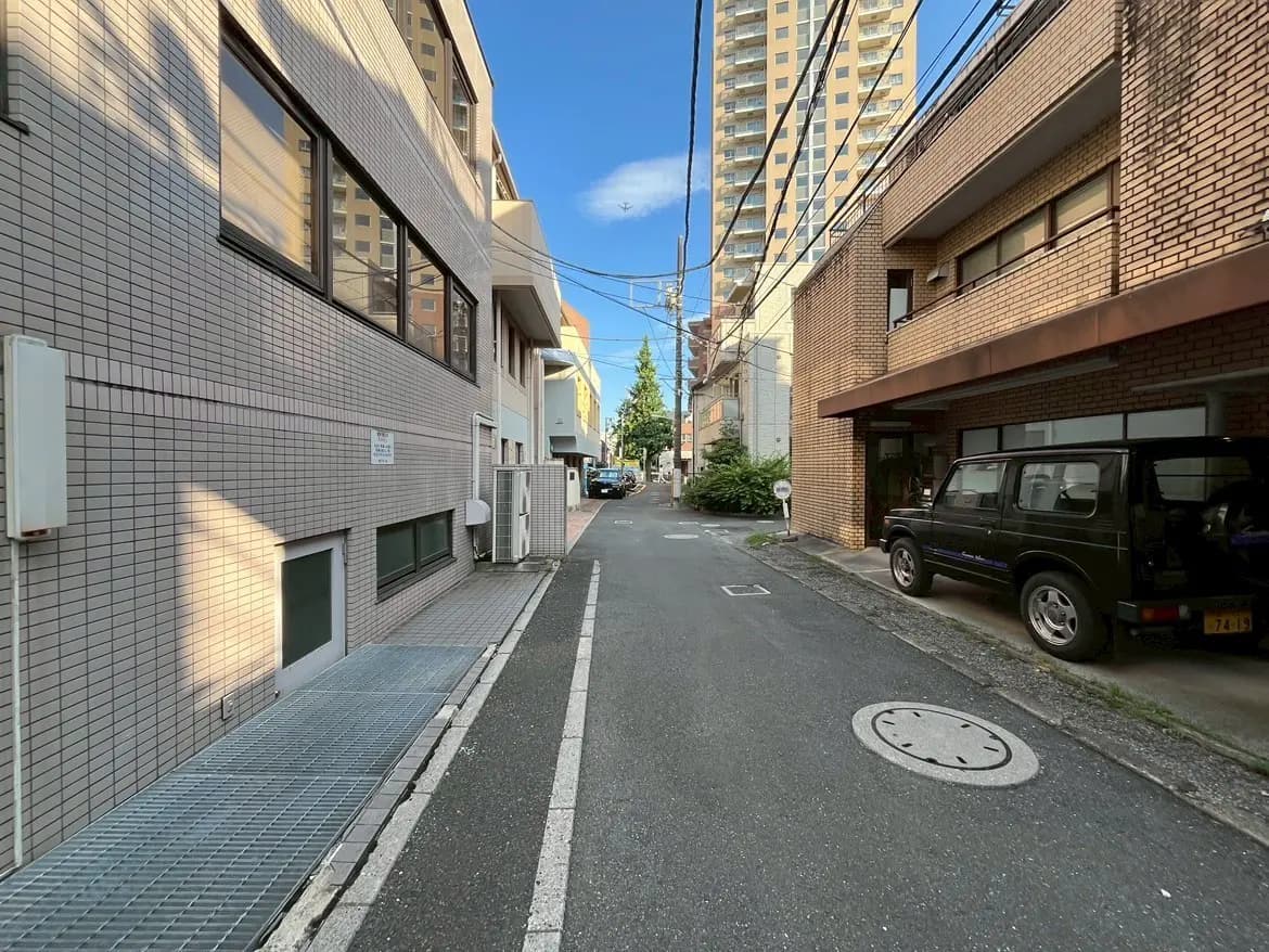 - 都市の住宅街の路地、レンガ造りの建物と近隣のマンションが並び、晴れた青空を背景にした風景