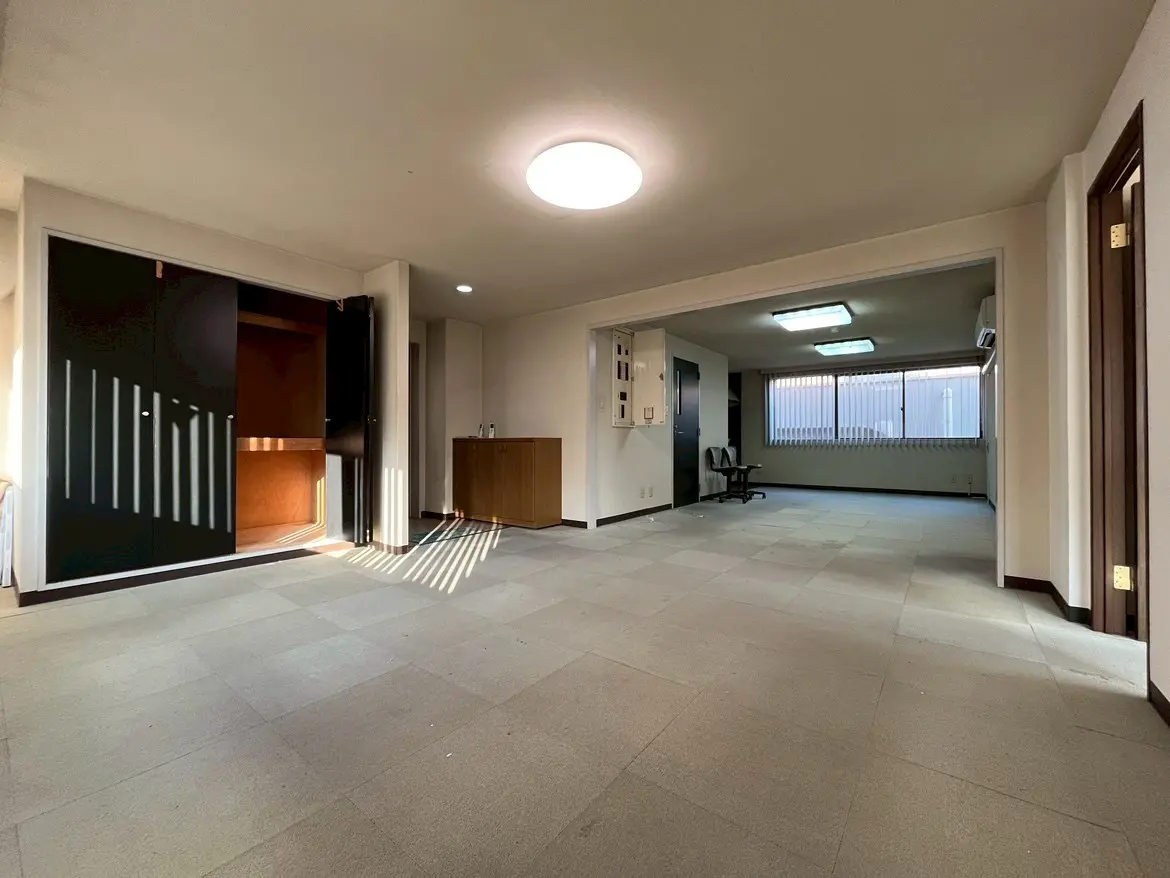 - 明るい照明が印象的な広々とした室内、スライドドアと収納スペース、シンプルなインテリアが特徴のリビングルーム