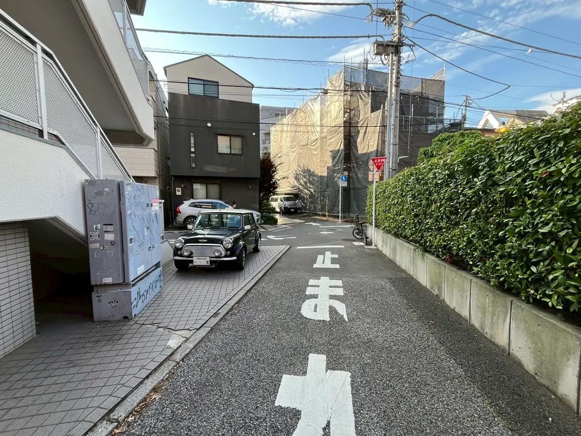 - 街中の住宅街の風景、舗装された小道に停車するクラシックなミニカーと高い建物の足場が見える景色