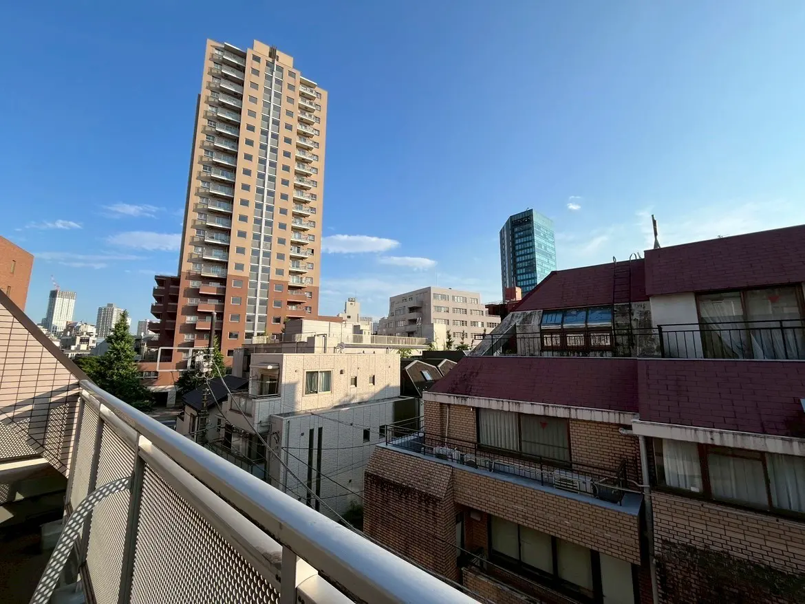 - 都市の高層ビル群を背景にしたバルコニーからの眺望、青空と建物の屋根が広がる風景