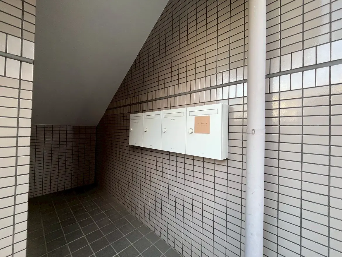 - 内部の郵便ボックスとタイル張りの壁が特徴的なアパートのエントランス、斜めの天井と落ち着いた色合いのインテリア