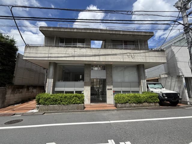 - コンクリート造のモダンな建物、広いガラス窓とエントランス、整えられた植栽と街並みの一部