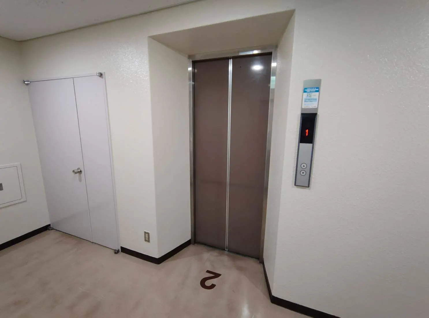 - エレベーターのドアがある建物の内部、横には階数表示パネルとその下にある「2」の文字が見えるエリア