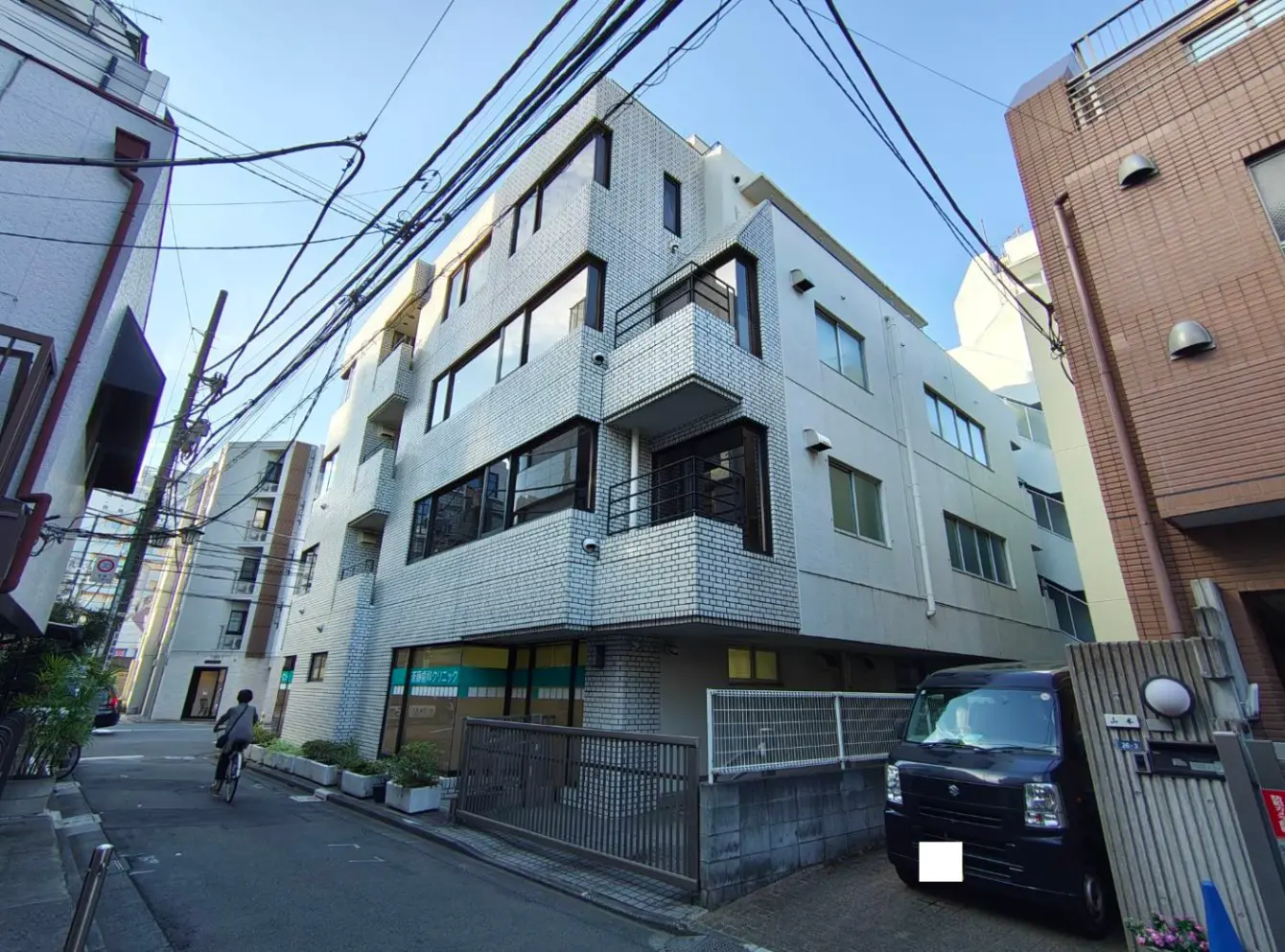 - モダンな外観のマンション、ホワイトタイルの壁、ガラスの窓、近くに自転車を押している人がいる住宅街の風景