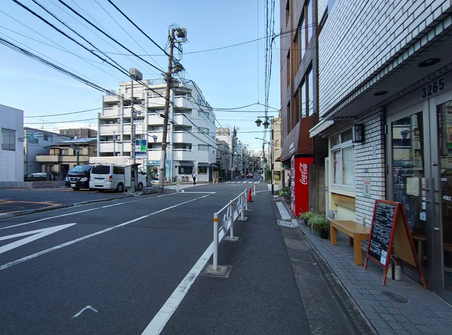 - 都市の街並み、交差点の様子、商業施設が並ぶ通りと電柱、コカ・コーラの自動販売機が見える風景