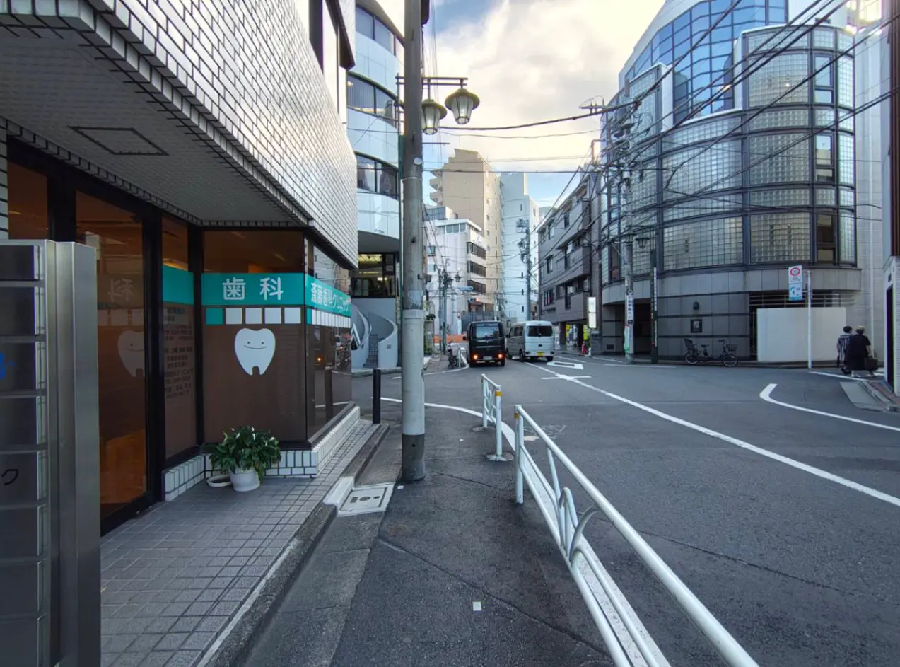 - 歯科医院の外観と周囲の街並み、白いタイルの壁とアートなデザインの建物が並ぶ通りの風景