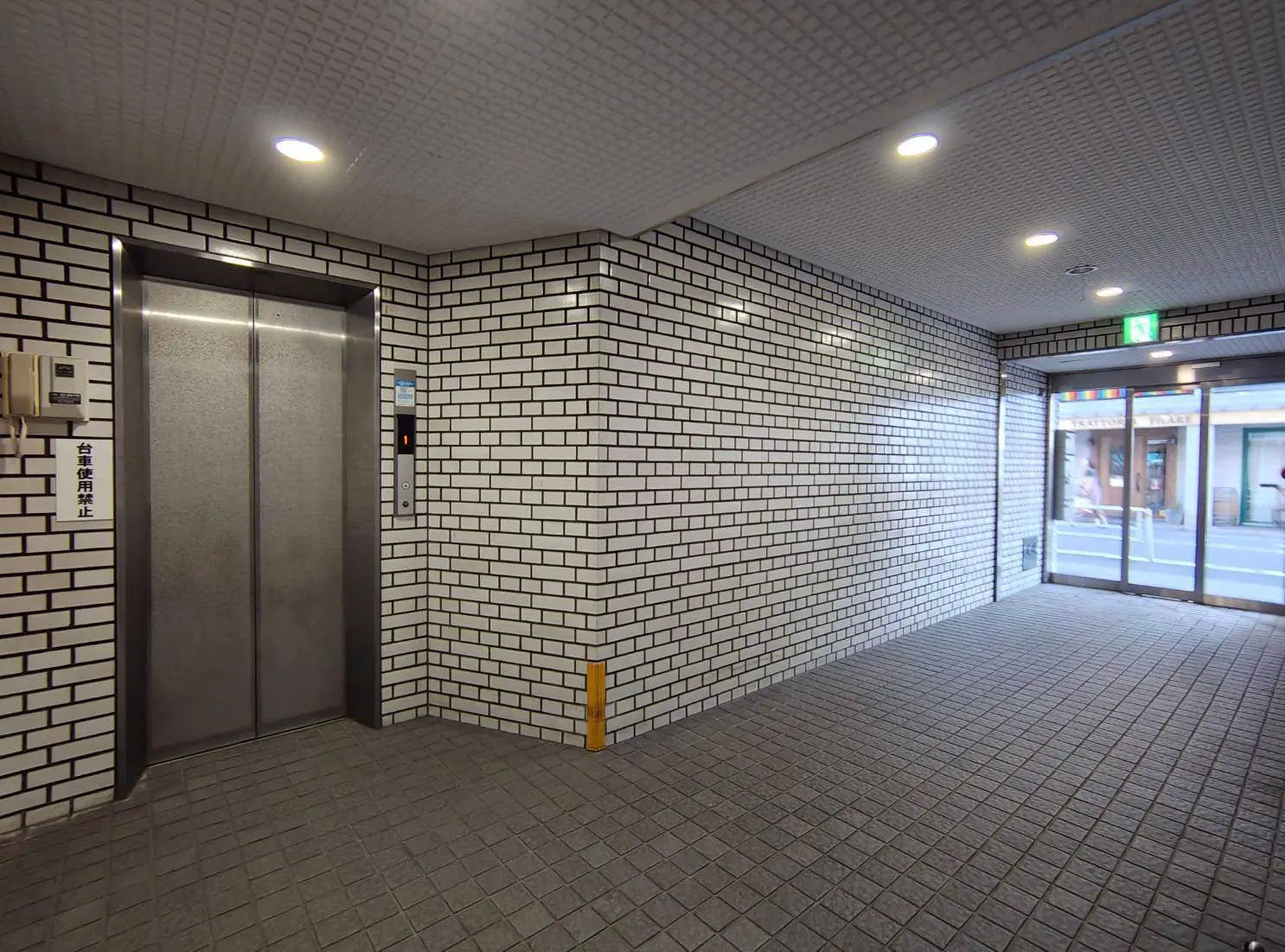 - 白レンガの壁とエレベーターがある現代的なエントランスホール、明るい照明とタイル張りの床が特徴的なインテリア