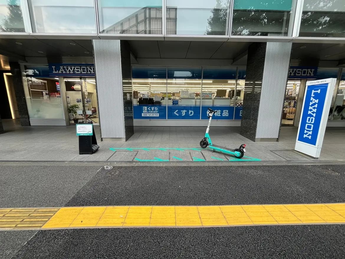 - コンビニエンスストア「ローソン」の店舗前に停まっている電動スクーター、歩道脇には利用規則の看板が設置されている様子
